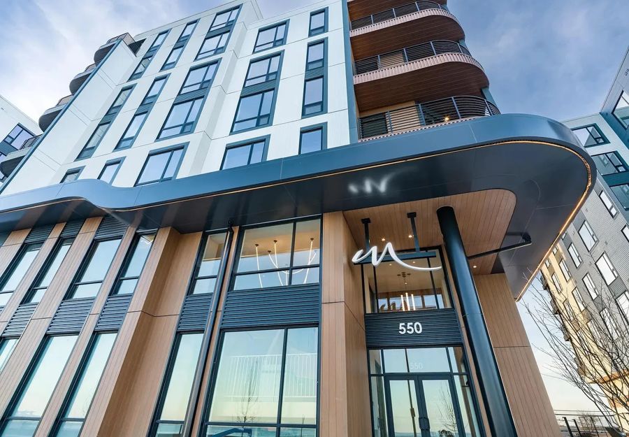 Building entrance with wood-tone cladding, white panels above and a curved metal canopy