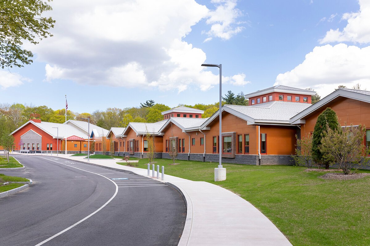 Early childhood education center seen from the driveway, with orange and red panel facades and gabled roofs